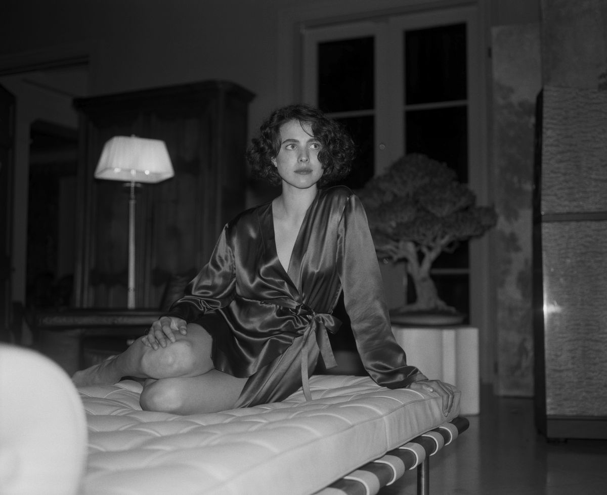 Margaret Qualley, skjuten i svart och vitt, vilar på en säng i en sidenmorgonrock i Kinds of Kindness