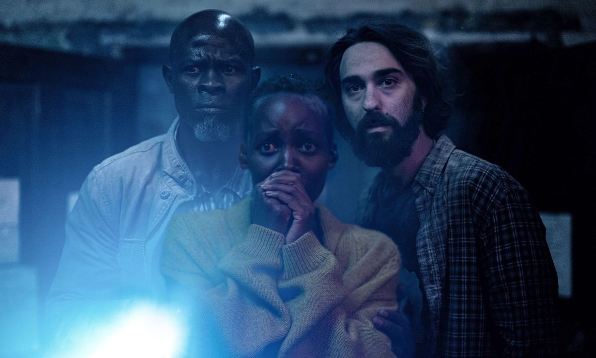 Tre överlevande från en utomjordisk invasion (Djimon Hounsou, Lupita Nyong'o, Alex Wolff) står tillsammans i mörkret och lyser med en ficklampa mot kameran i Michael Sarnoskis A Quiet Place: Day One