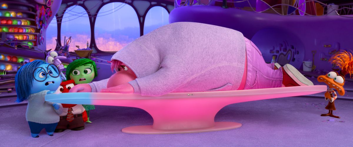 Embarrassment, en stor, blobbig, rosa kille i en grå luvtröja, ligger utspridda över kontrollbrädan i känslor HQ när de andra karaktärerna står och ser oroliga ut i Pixar Animation Studios Inside Out 2