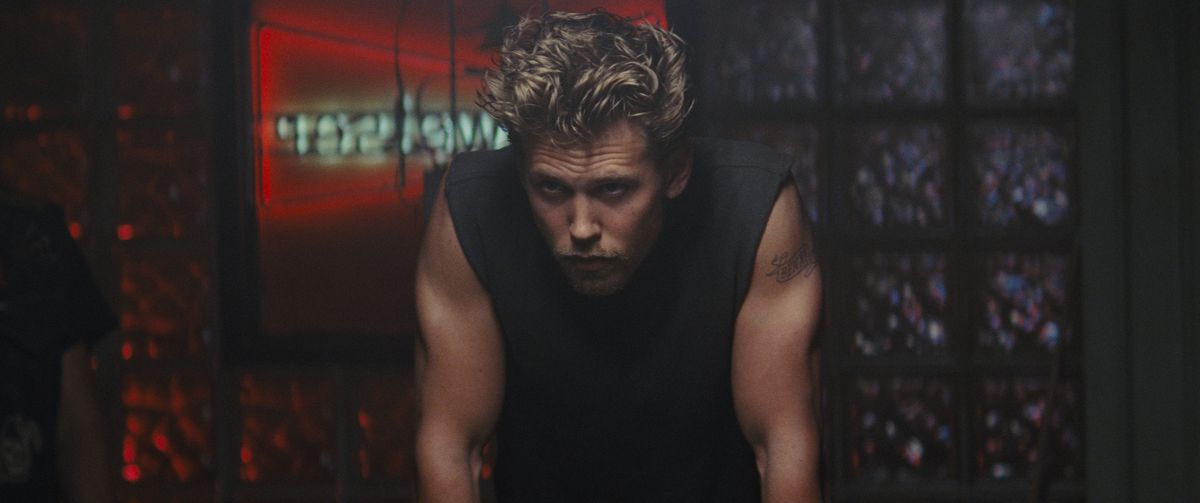 Austin Butler, med hårt hår, klädd i en svart ärmlös topp, lutar sig fram på ett lynnigt sätt i The Bikeriders