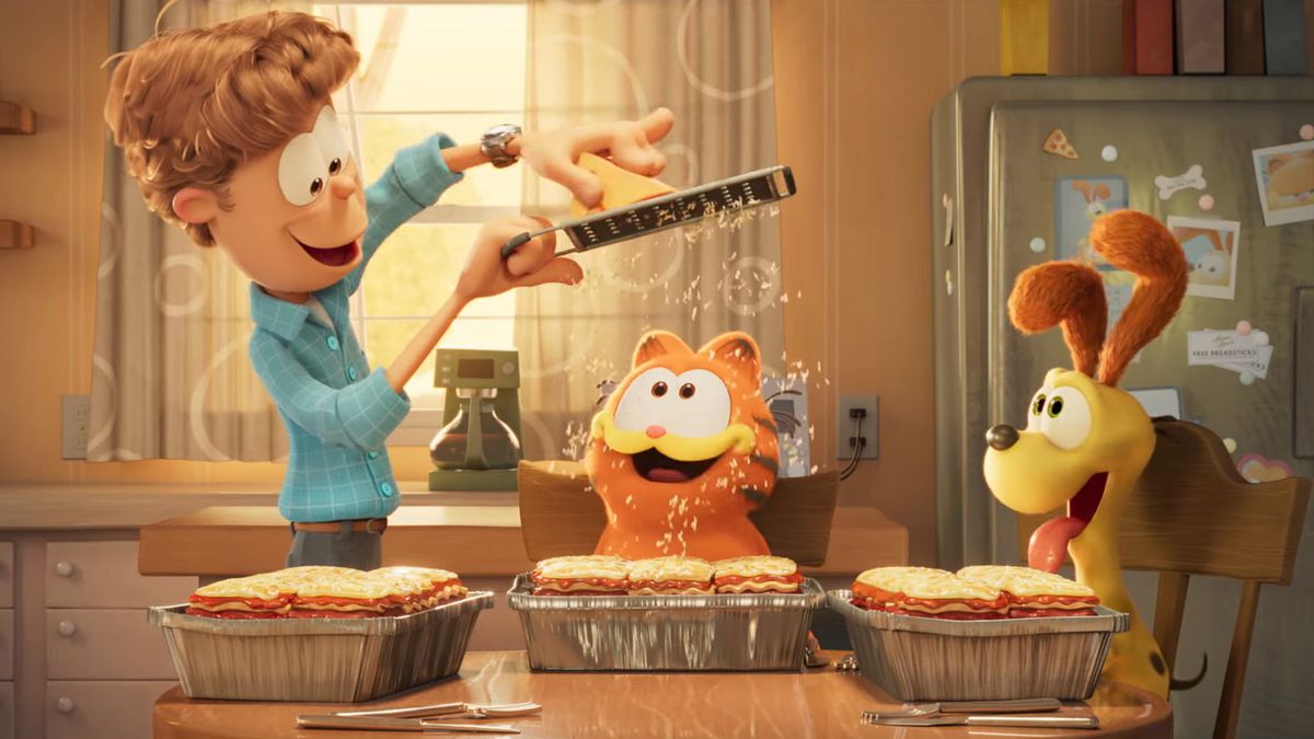 Jon Arbuckle rakar parmesanost över Garfields lasagne medan Odie tittar i en stillbild från The Garfield Movie