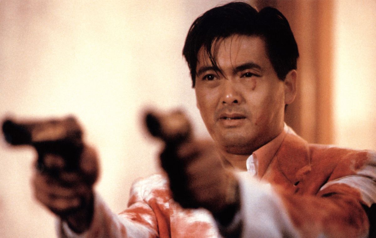 Chow Yun-fat, wearing a bloodied suit, holds up two pistols in The Killer