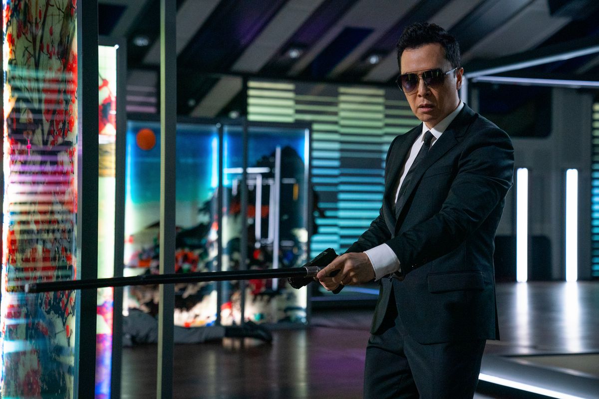 Donnie Yen, wearing a suit and sunglasses, holds out a gun and a cane in John Wick: Chapter 4.