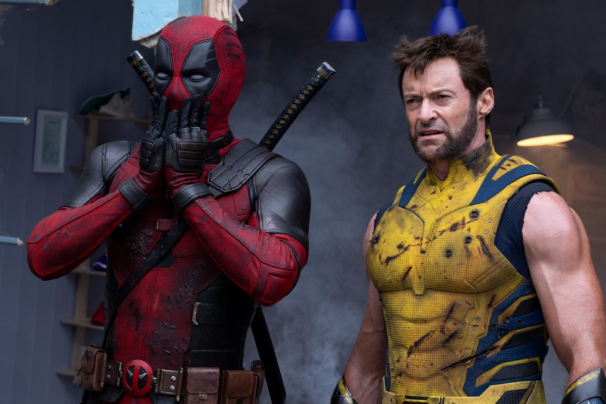 En stridsärrad Deadpool lägger händerna över sin mun i chock när en misshandlad Wolverine ser trött ut bredvid honom i en scen från filmen Deadpool & Wolverine